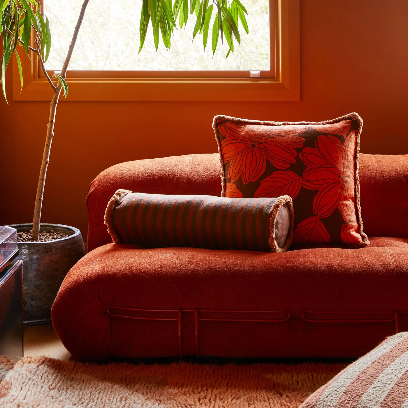 Living room with sofa and floral cushion, and Boucle Stripe Chocolate Pouffe