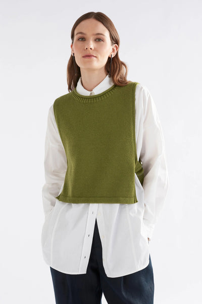 Woman wearing black pants, white button down long sleeve shirt and miraa vest in artichoke colour