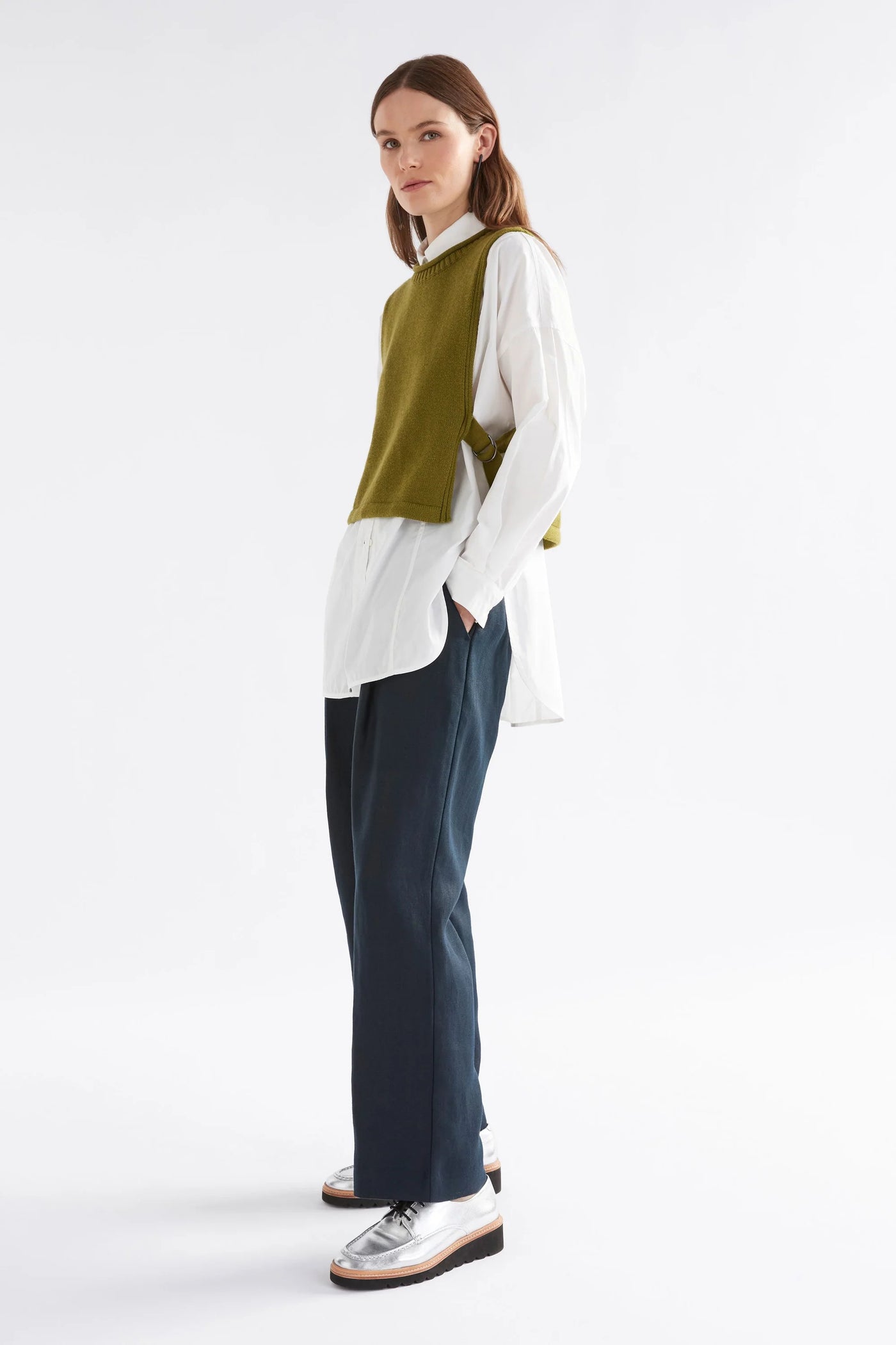 Woman wearing black pants, white button down long sleeve shirt and miraa vest in artichoke colour