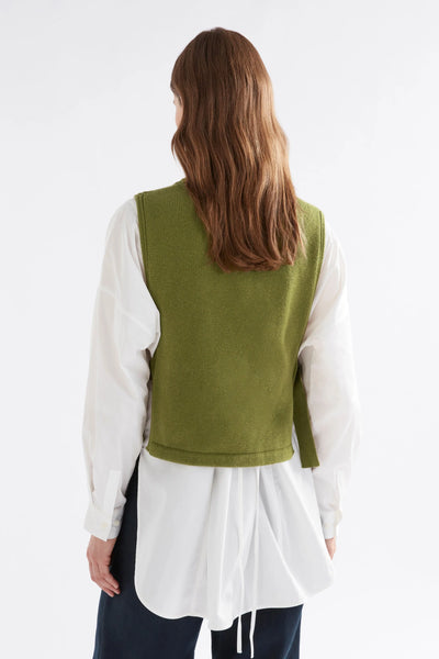 Woman facing back wearing black pants, white button down long sleeve shirt and miraa vest in artichoke colour