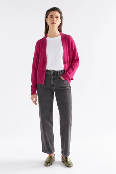 Woman wearing white top, bright pink cardigan and black jeans