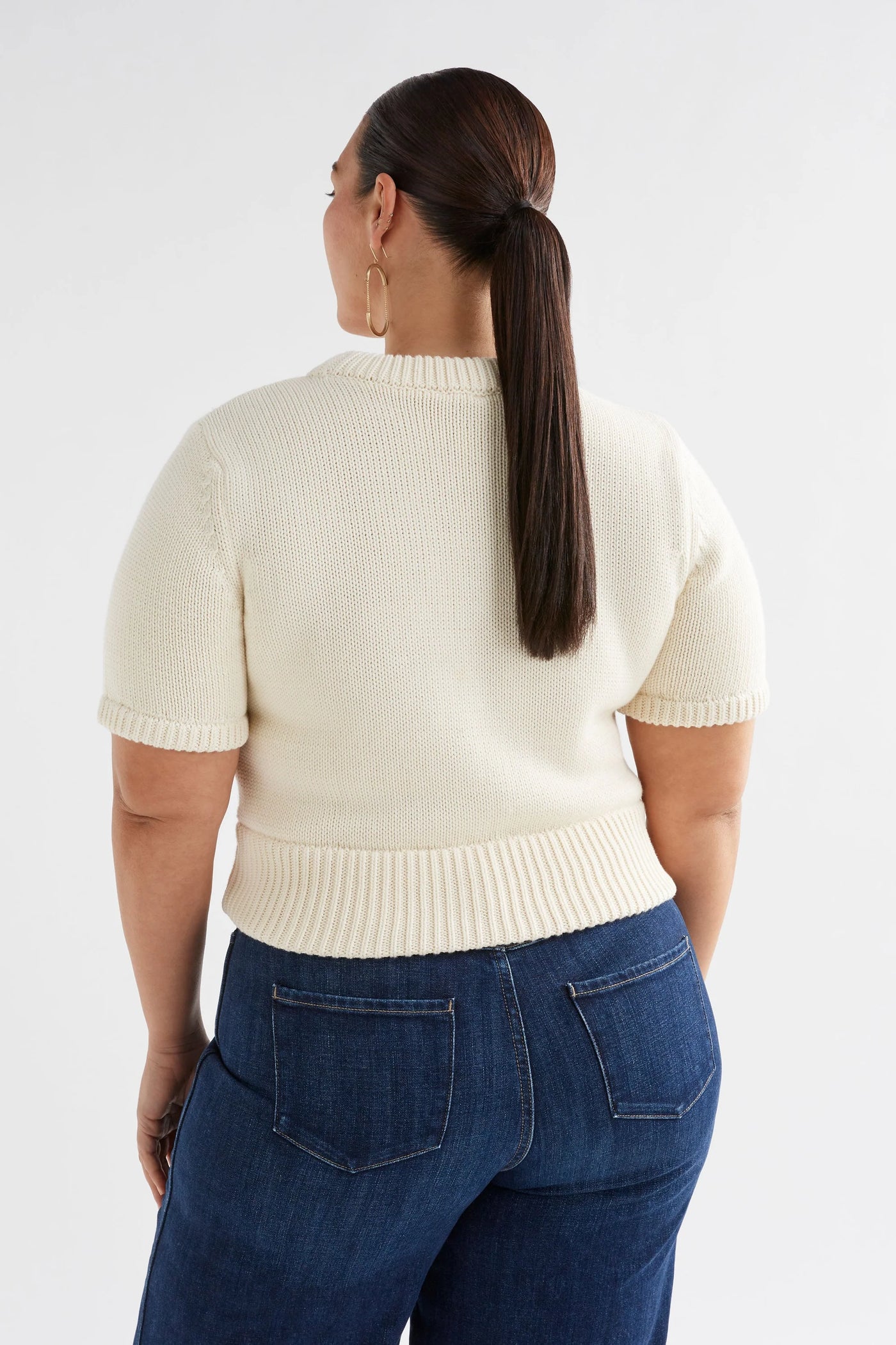 Plus size woman facing the back wearing Luft Knit Top in White and Dark Blue Denim pants