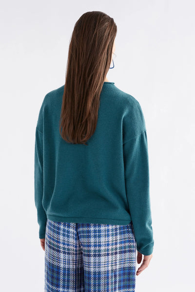 Woman facing the back wearing Pirata Sweater in Sea Moss and Blue plaid bottoms