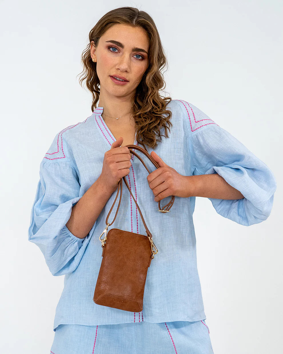 Woman holding the Elm and King Sullivan Phone Bag in Tan Pebble