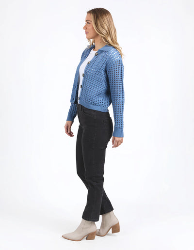 woman facing the side wearing Clover Knit Cardi in Coronet Blue, white top and denim skirt