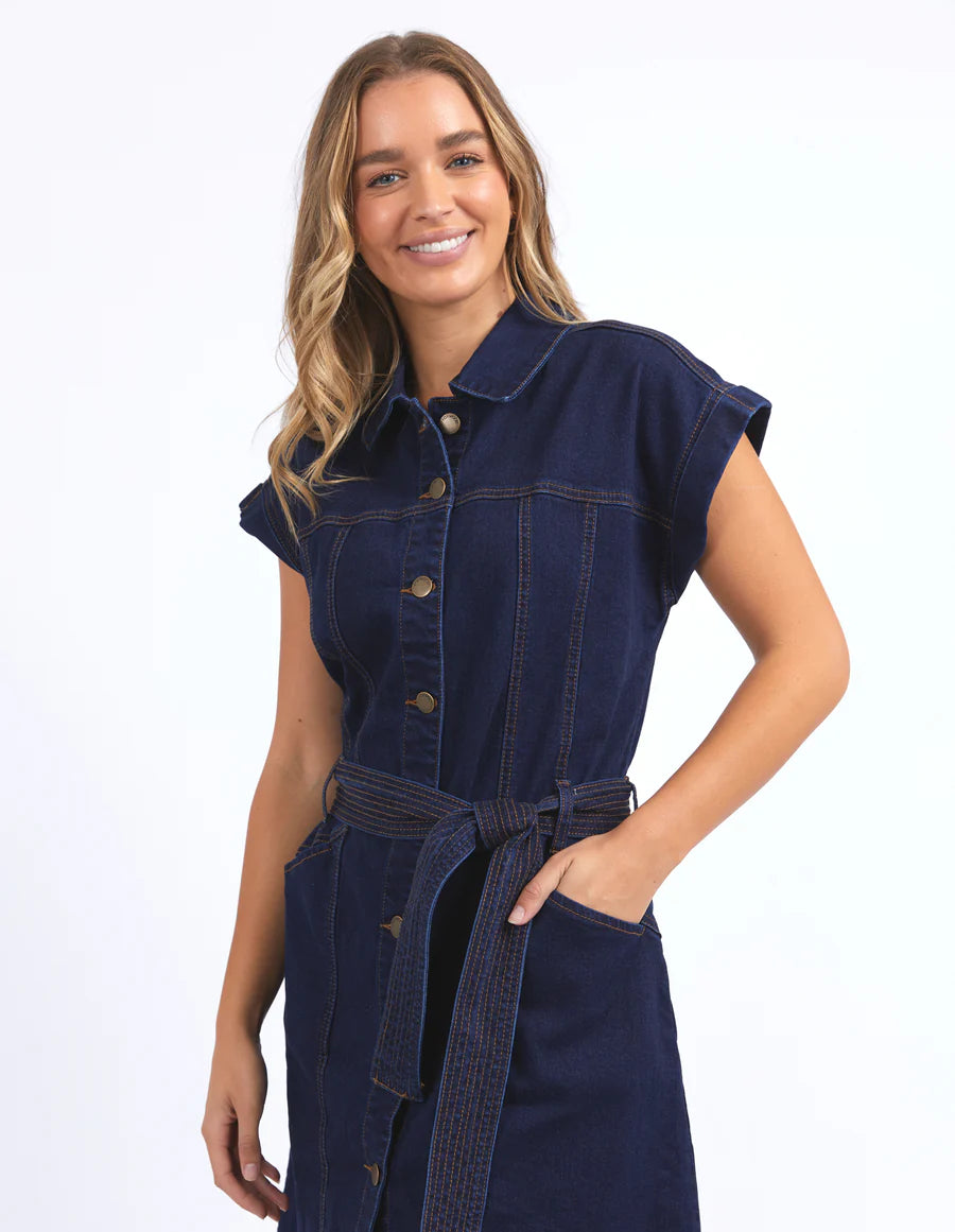 Woman wearing foxwood heidi dress in dark blue denim while hand on the pocket