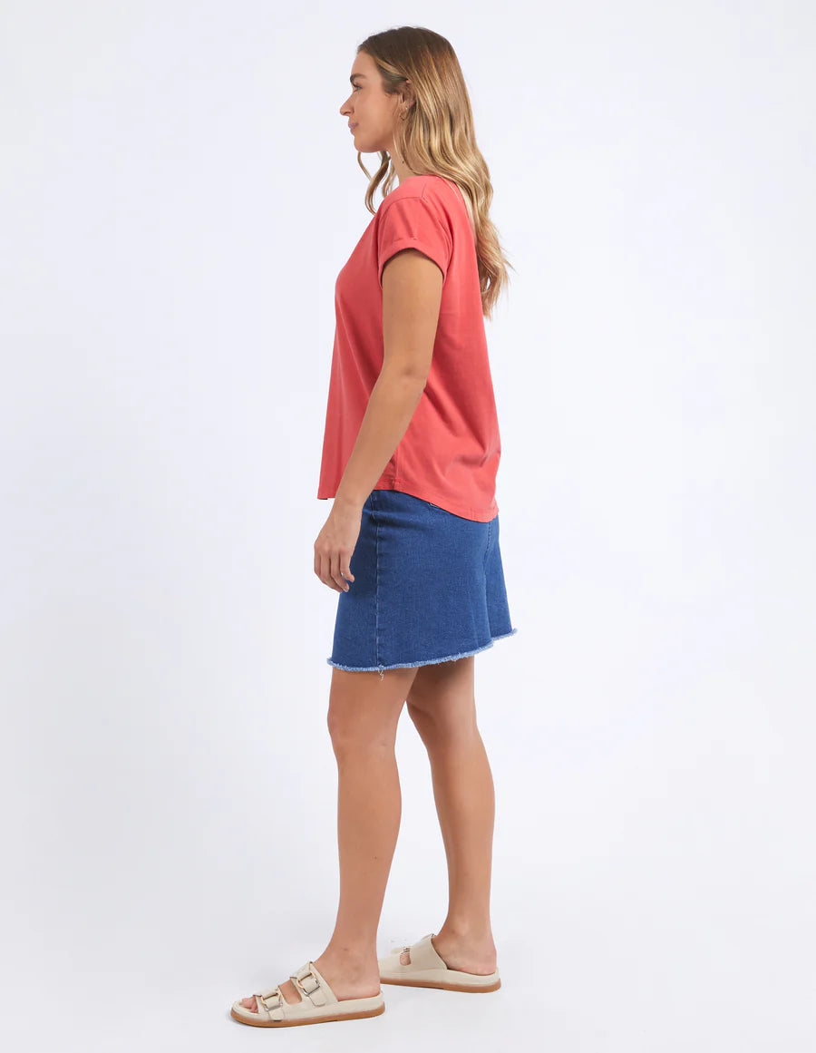 Woman wearing  foxwood manly vee tee in cayenne colour and blue denim skirt and slip on