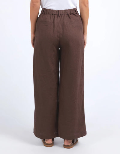 woman facing the back wearing white sleeveless top and foxwood pierra pants in chocolate colour