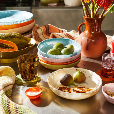 A collection of sage and clare toni bowl in different colour and sizes, displayed on a kitchen counter with fresh fruits